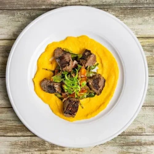 Seared meat, greens, and yellow purée on a white plate.