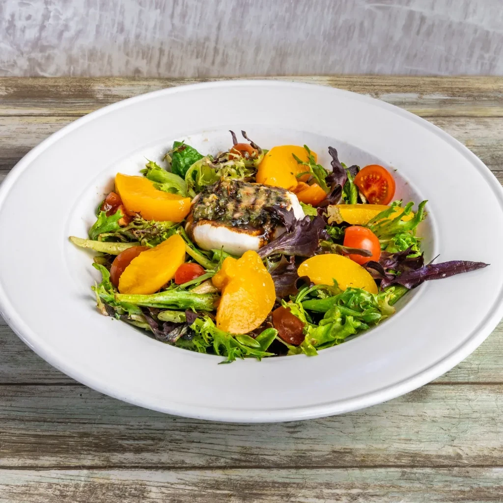 Salad with lettuce, fruit, tomatoes, and burrata on a wooden surface.