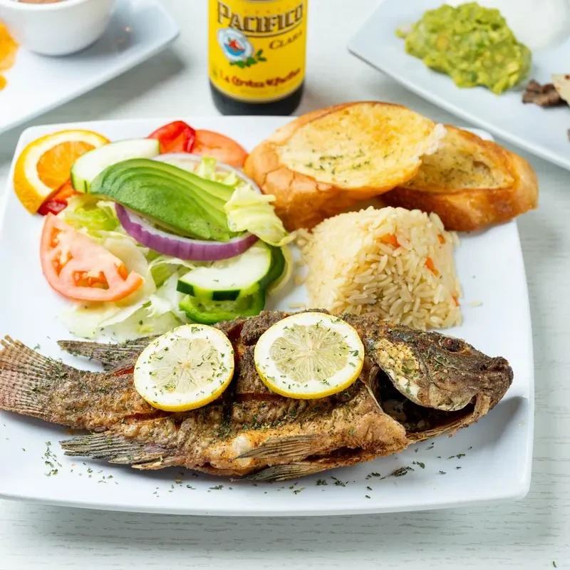 A white plate with fried fish, salad, rice, and garlic bread.