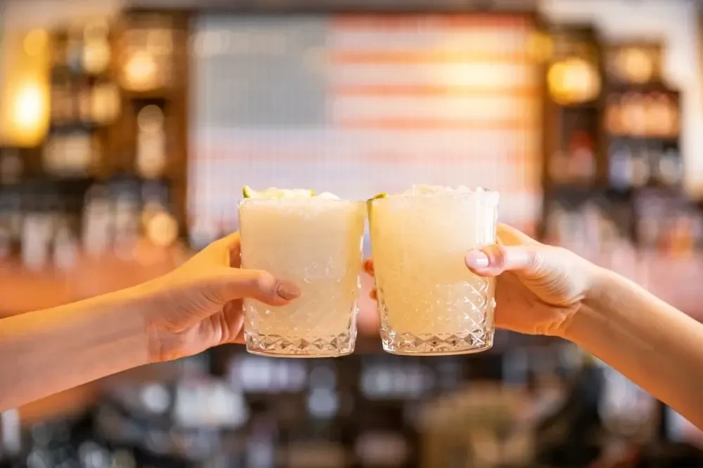 Two hands holding clear glasses of a light-colored drink.