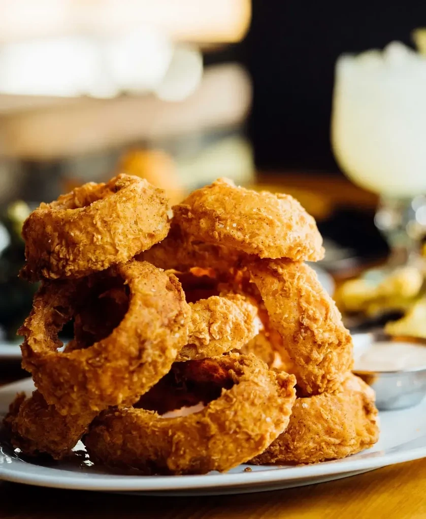 Large stack of golden-brown, heavily breaded onion rings on a white plate.