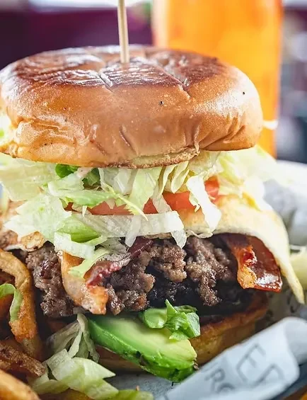 Gourmet burger with avocado, bacon, and fries on a wooden table.
