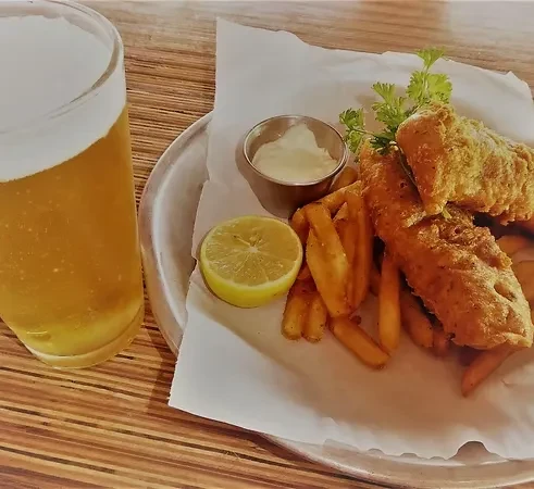 Fish and chips with tartar sauce, lemon, and a glass of beer.