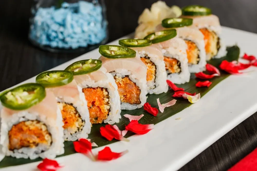 Eight sushi rolls topped with fish and jalapeño on a white plate.