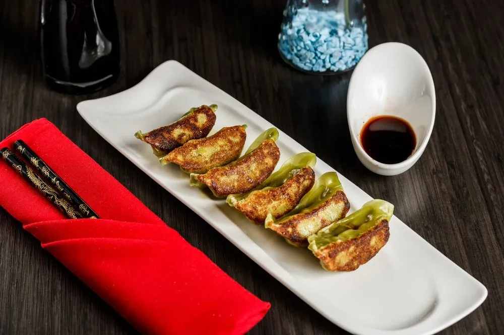 Six pan-fried vegetable dumplings, sauce, chopsticks, and a napkin.