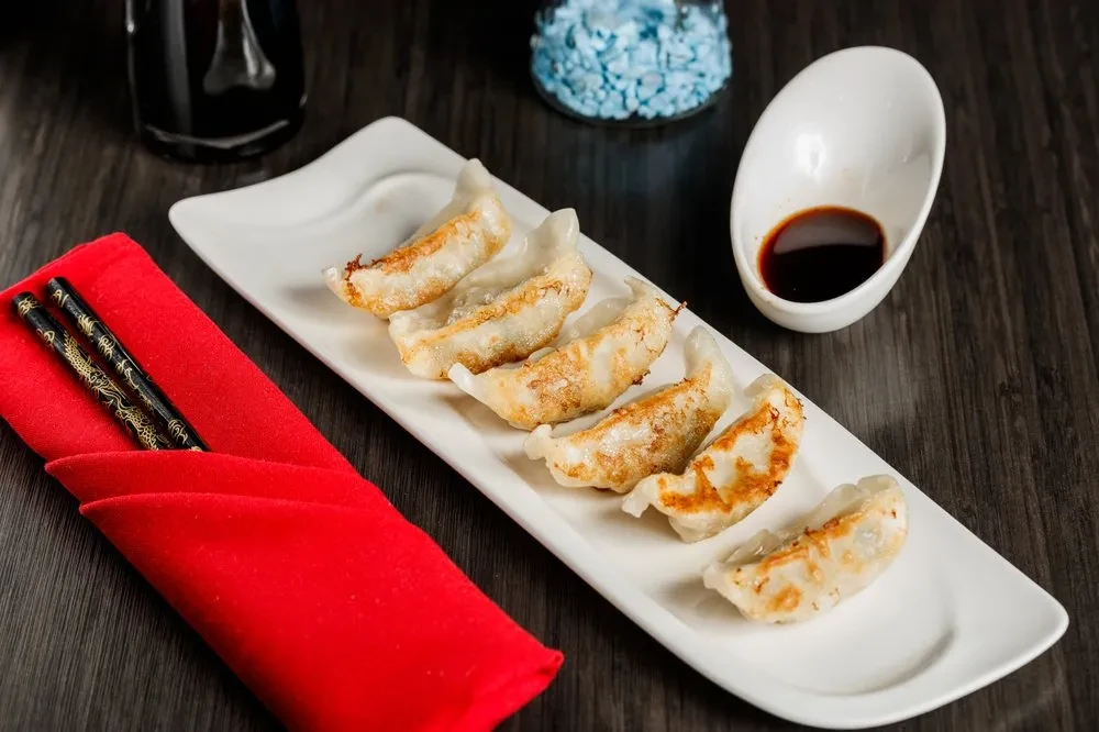 Pan-fried dumplings, chopsticks, and dipping sauce on a wooden table.