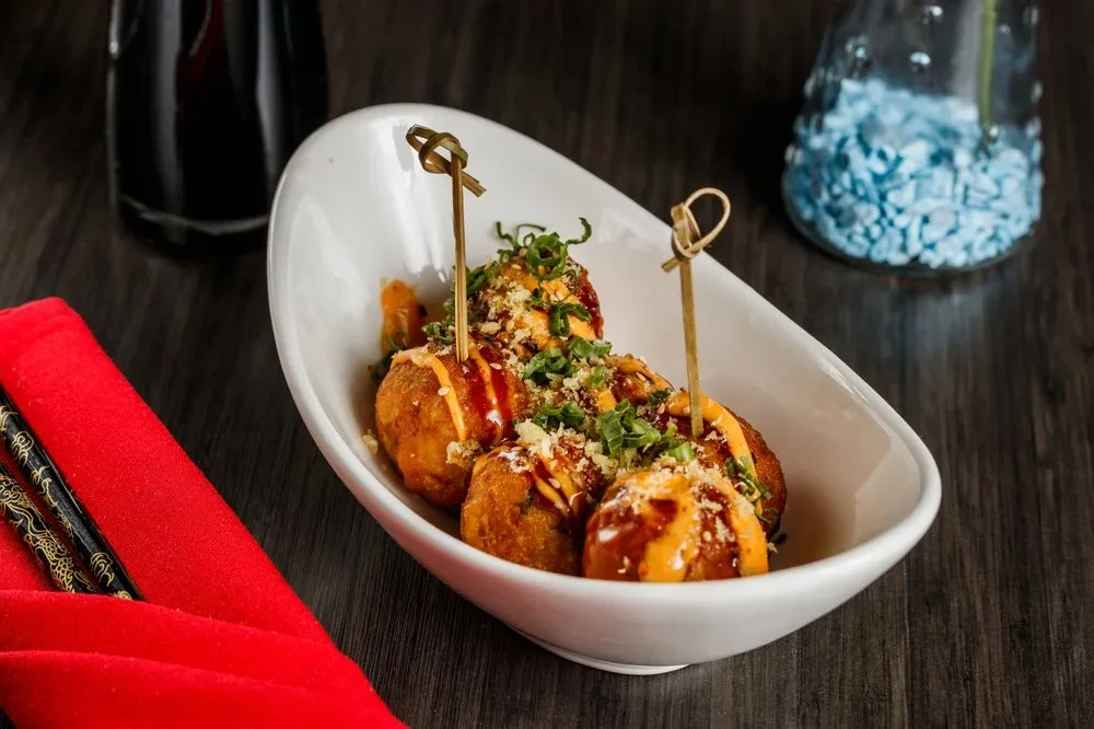 Golden-brown spherical food with sauces and herbs in a white bowl.