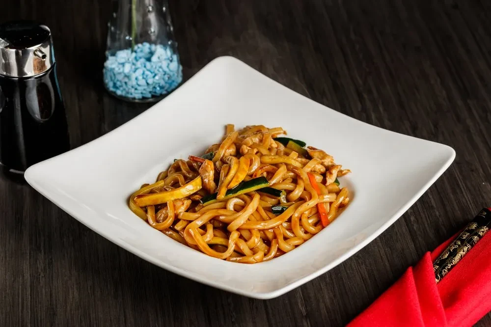 Stir-fried noodles with chicken and vegetables in a white bowl.