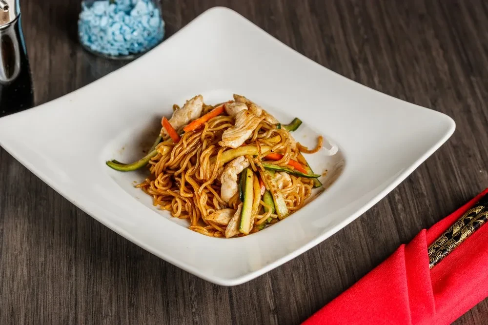 Stir-fried noodles with chicken, carrots, and zucchini in a white plate.