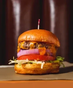 Gourmet cheeseburger with brioche bun, two patties, cheese, onion, tomato, lettuce.