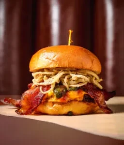 Gourmet burger with bacon, melted cheese, peppers, and fried onions.