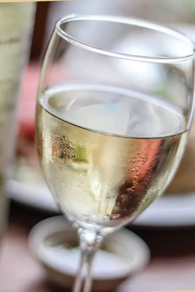 Close-up of a wine glass filled with cold, pale yellow liquid.