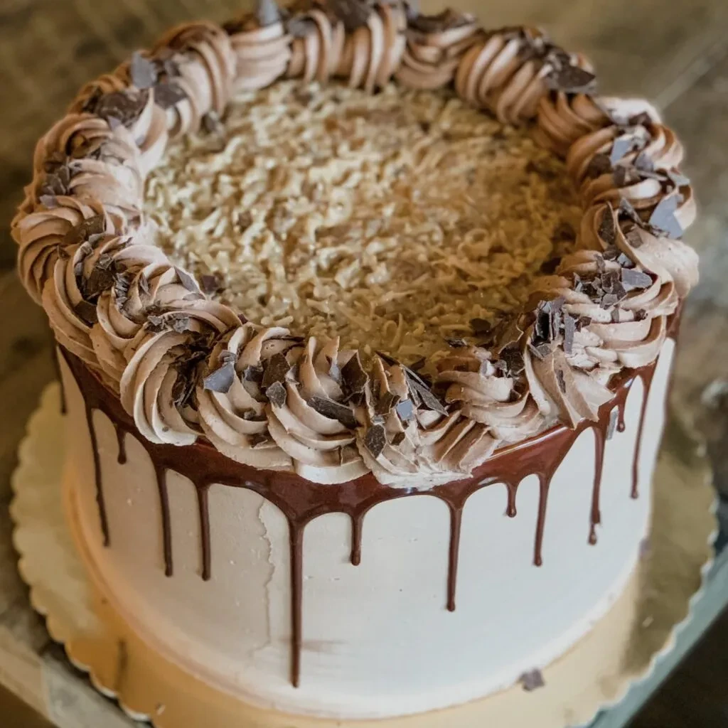 Round cake with chocolate ganache, frosting swirls, and shavings.