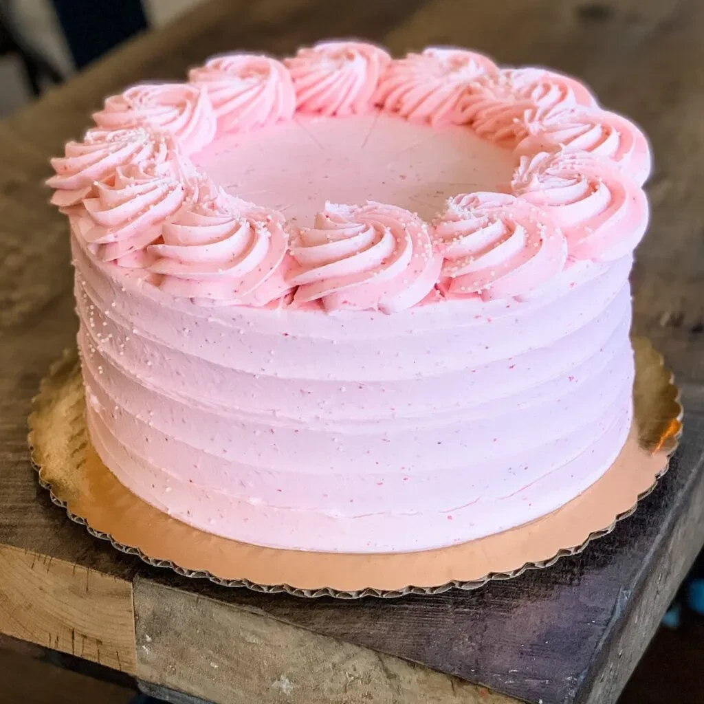Round pink cake with ridged frosting, rosettes, and sprinkles.