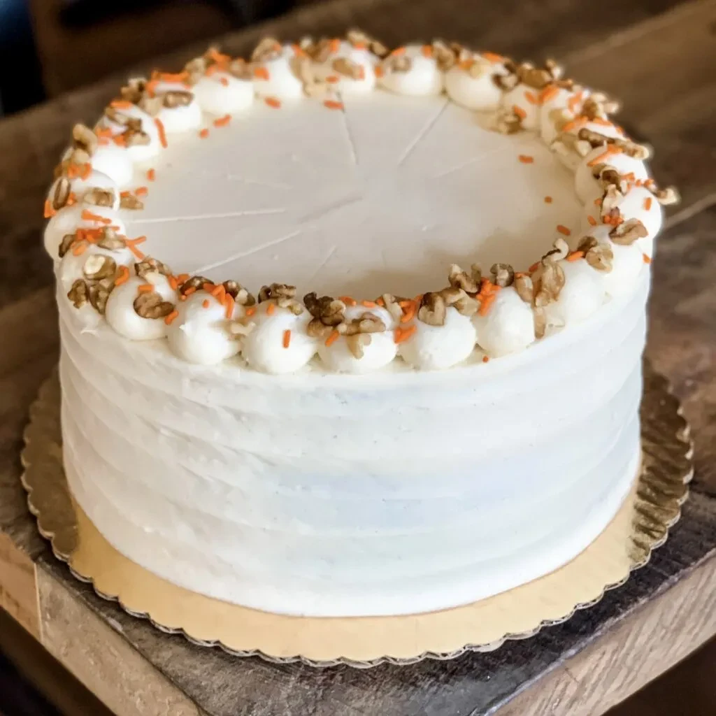 Round cake with walnuts, orange sprinkles, and white frosting.