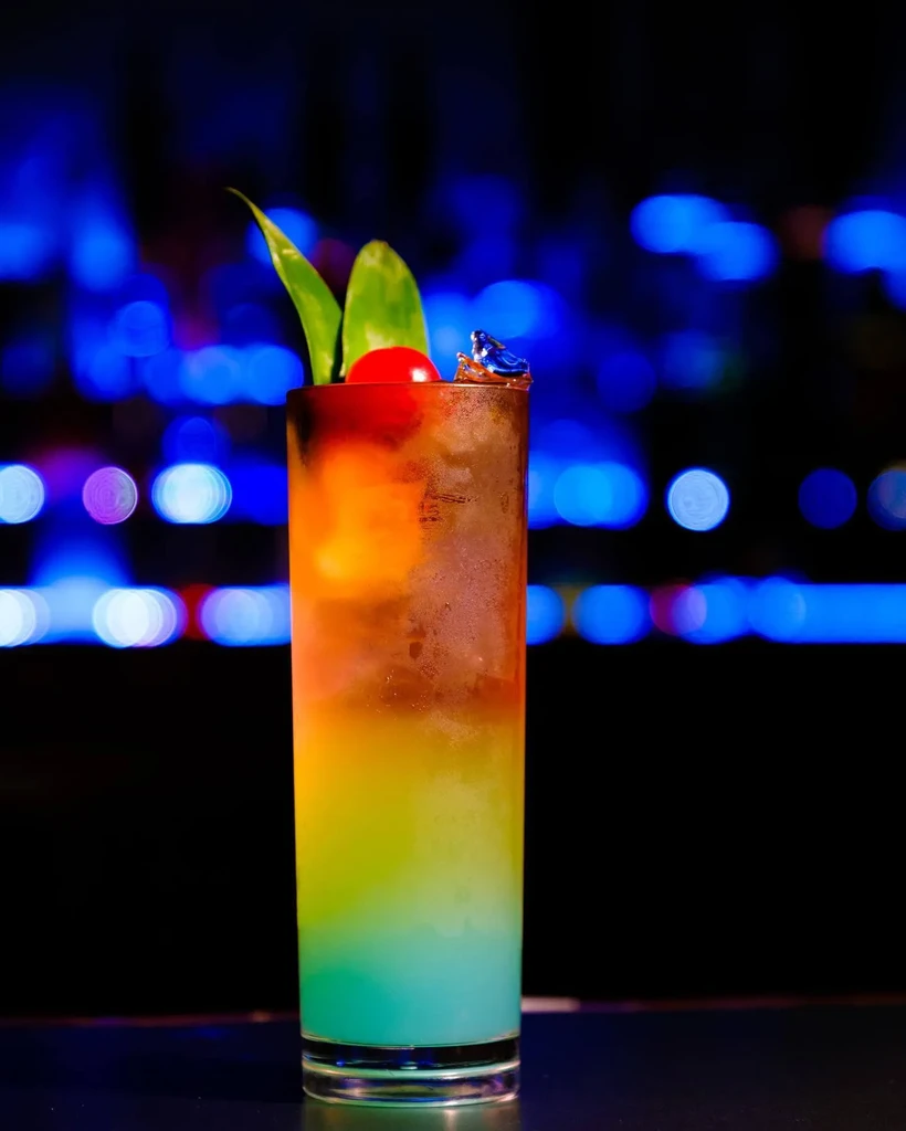Layered cocktail with amber, yellow, green, and blue colors, garnished.