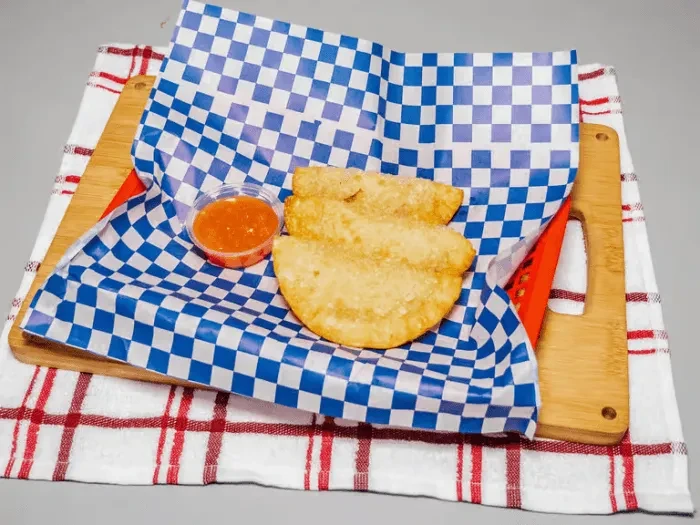 Three fried crescent pastries with sauce in a red basket.