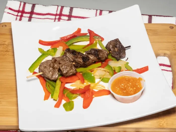Grilled meat skewers, stir-fried vegetables, and dipping sauce on a plate.
