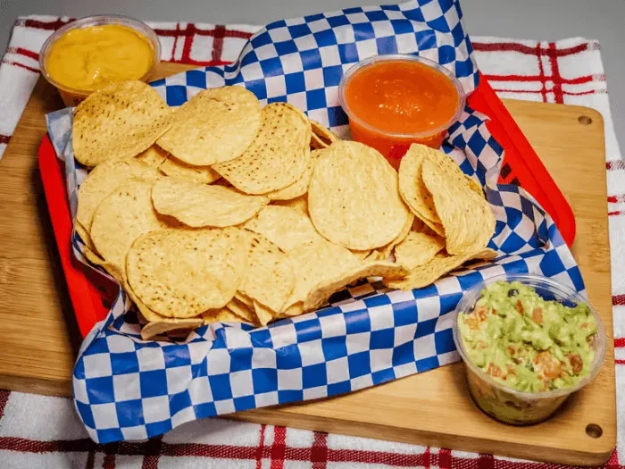 Tortilla chips in a basket with cheese, salsa, and guacamole.