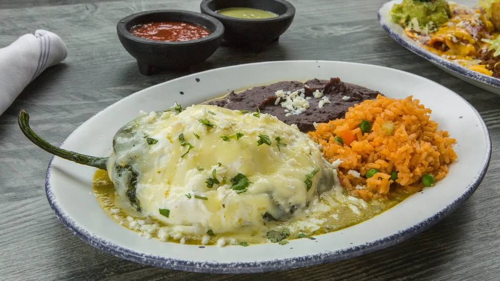 Chile relleno with rice and beans on a wooden table.
