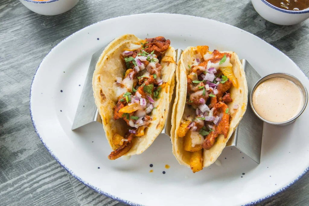 Two generously filled tacos with meat, cheese, onions, and cilantro.
