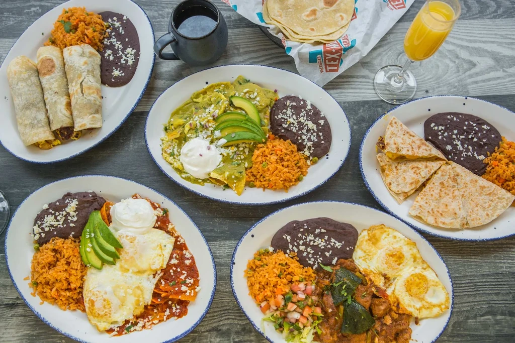 Five plates of Mexican-style food on a dark wooden table.
