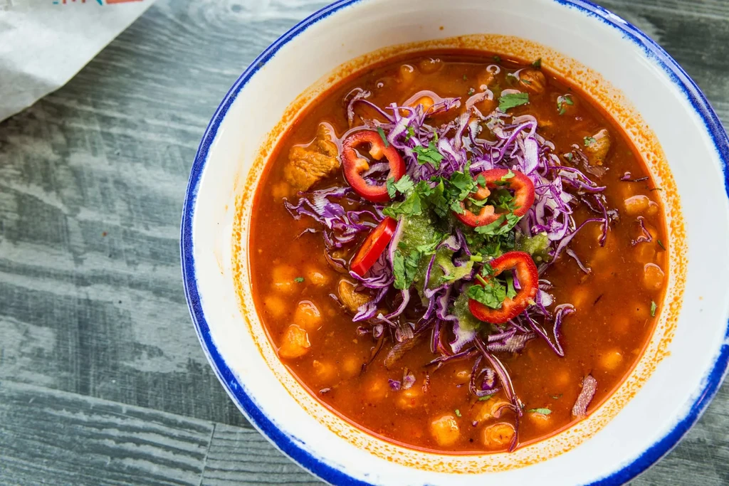 Overhead shot of a vibrant bowl of pozole on a wooden table.