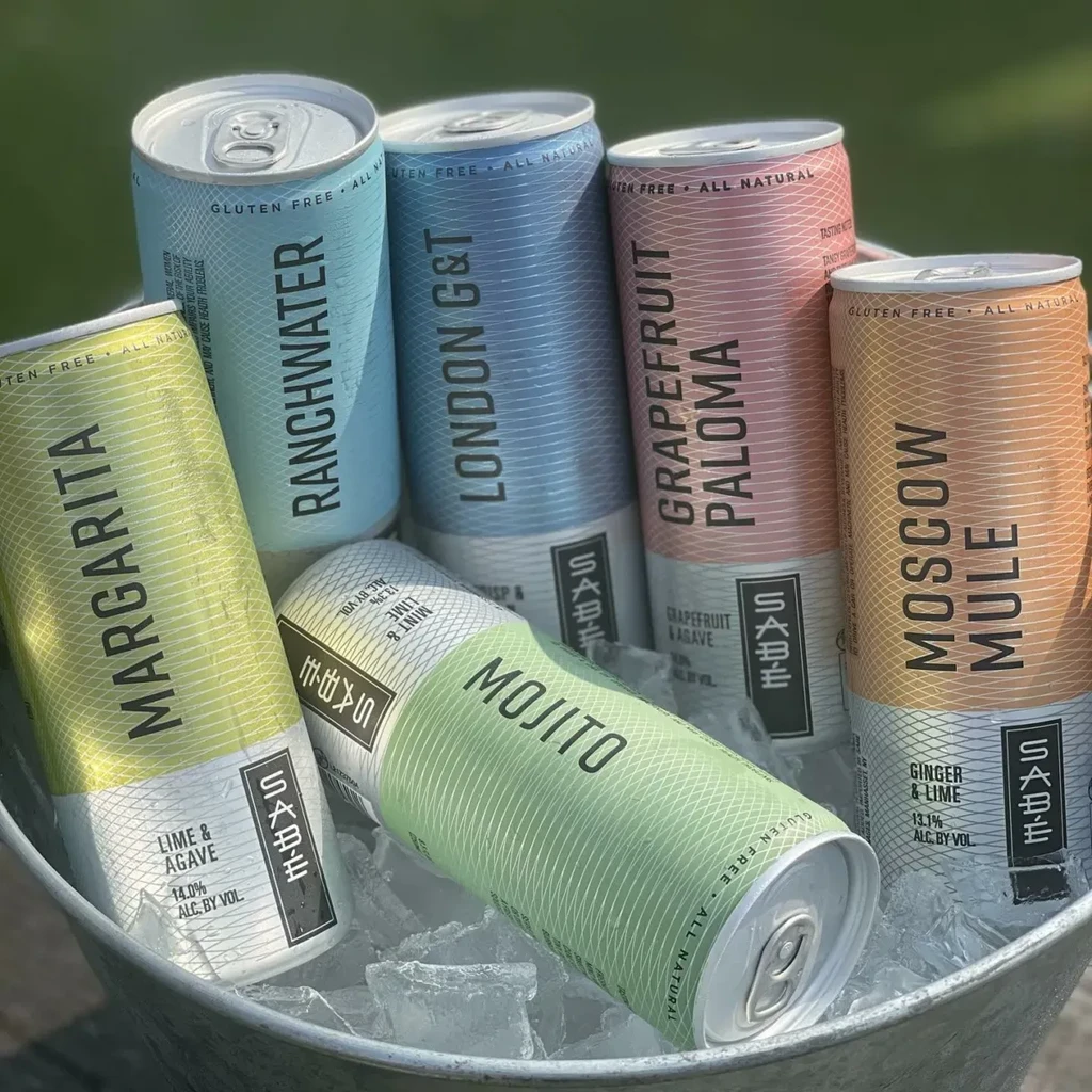 Six colorful cocktail cans chill in an ice bucket.