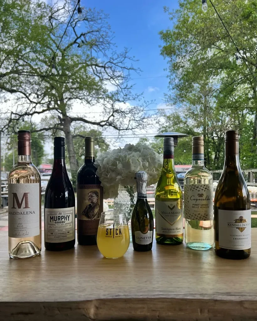 Wine bottles, a cocktail, and flowers on an outdoor table.