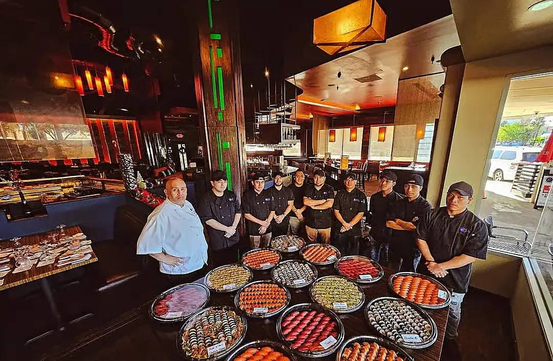 Restaurant staff standing behind large sushi platters in dining room