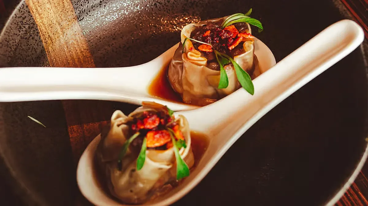 Two dumplings on white ceramic spoons in dark bowl
