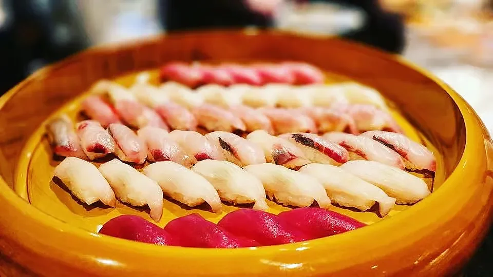 Assorted nigiri sushi arranged in round wooden serving bowl