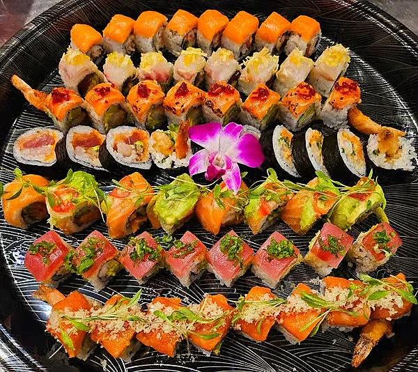 Large platter of assorted sushi rolls garnished with purple orchid