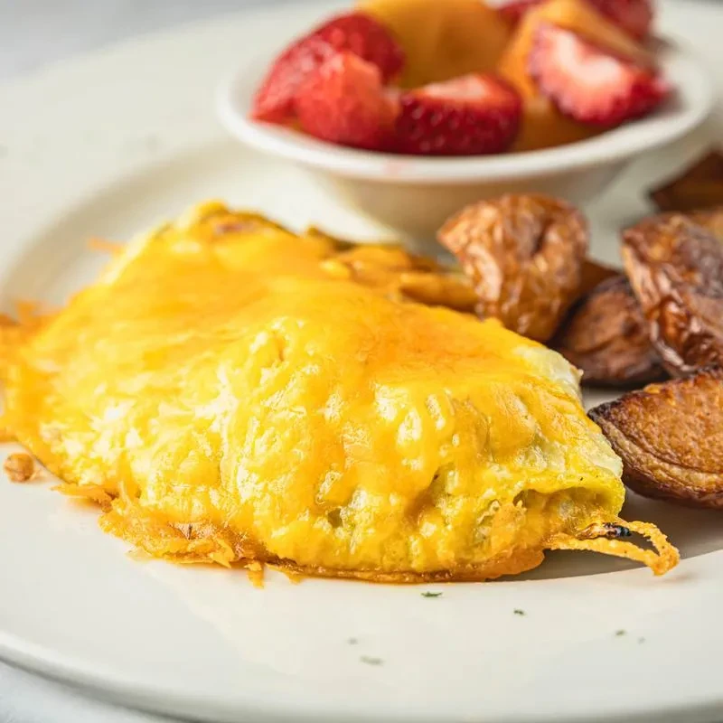 Breakfast plate with a cheese omelet, roasted potatoes, and fruit salad.