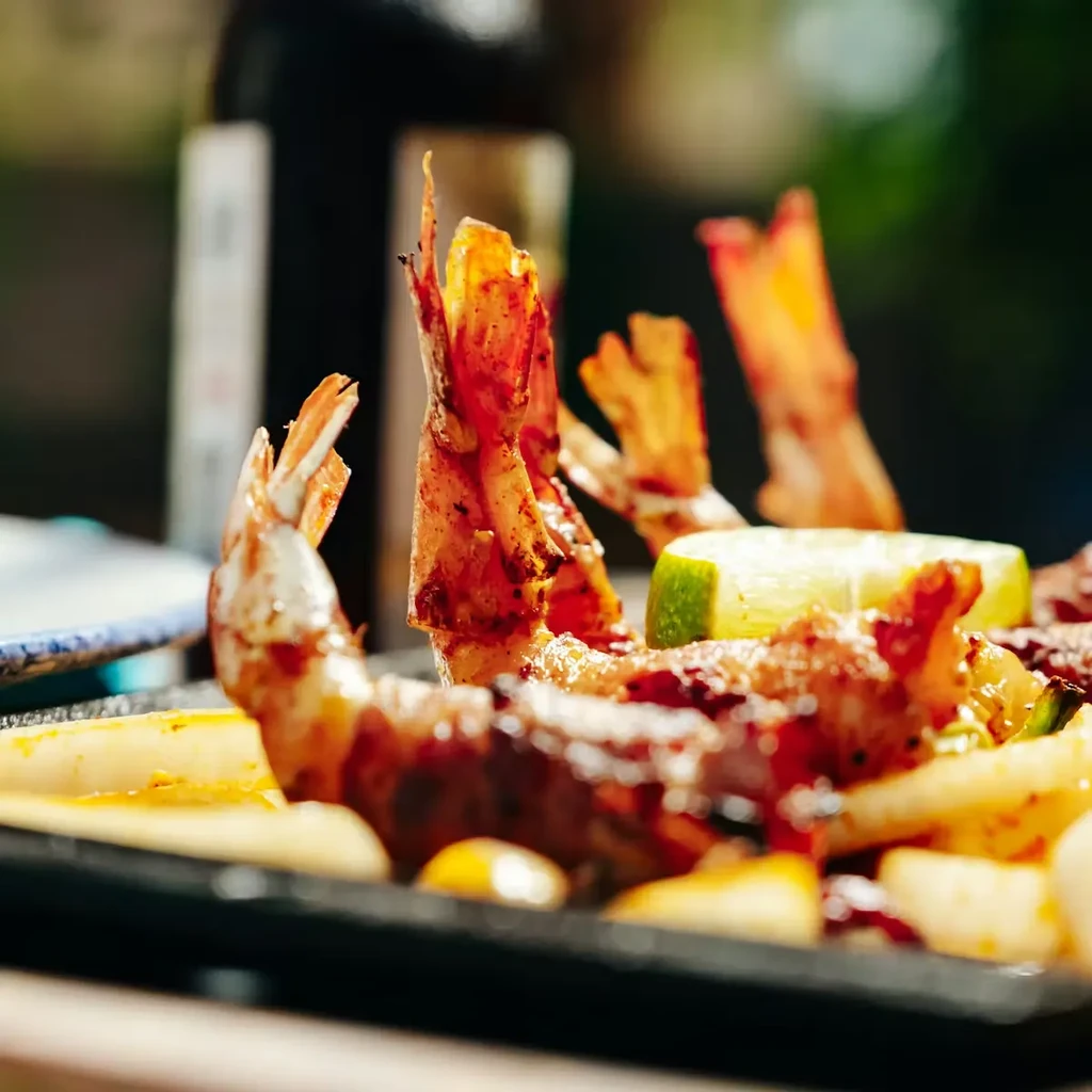 Grilled shrimp tails, lime, and other ingredients on a black platter.