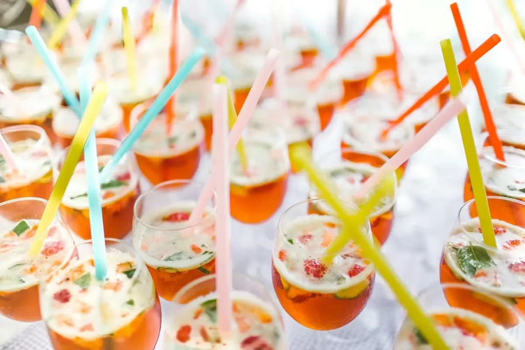 Close-up of orange drinks with fruit, herbs, and colorful straws.