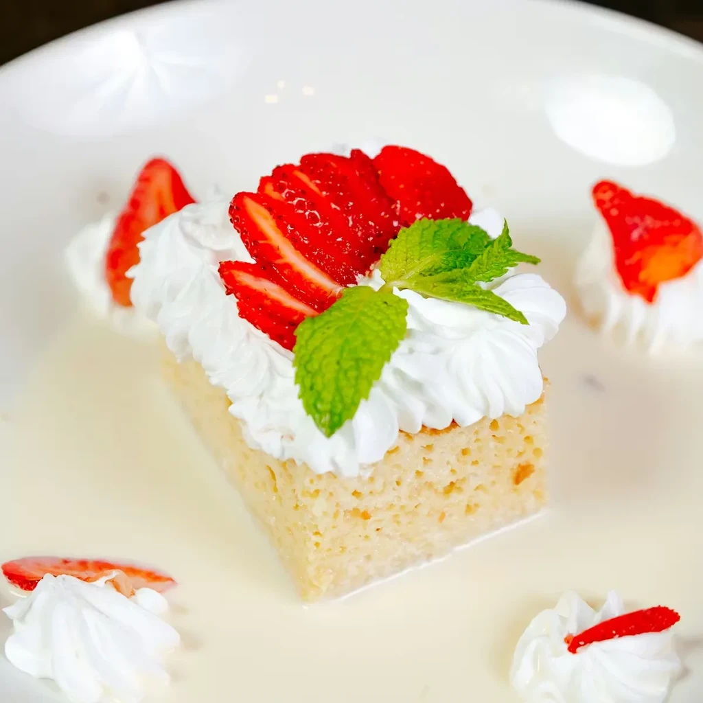 Tres Leches cake slice with whipped cream, strawberries, and mint.