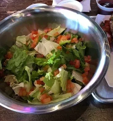 Large metal bowl filled with fresh green lettuce and red tomatoes.