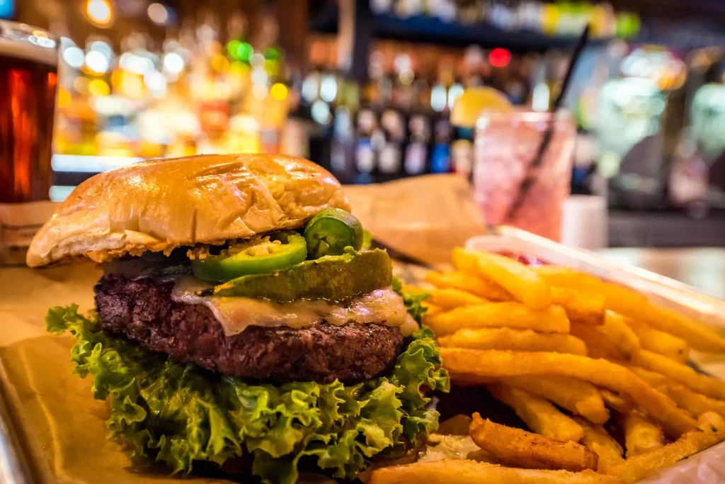 Gourmet burger with jalapeños and fries on a tray.