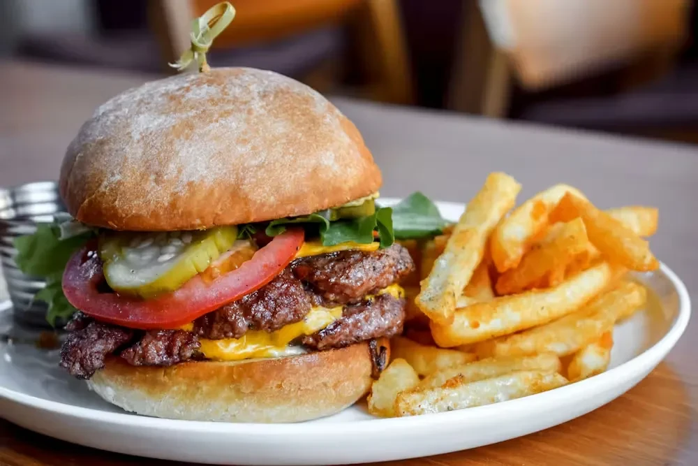 Double cheeseburger with tomato and pickles, side of french fries.