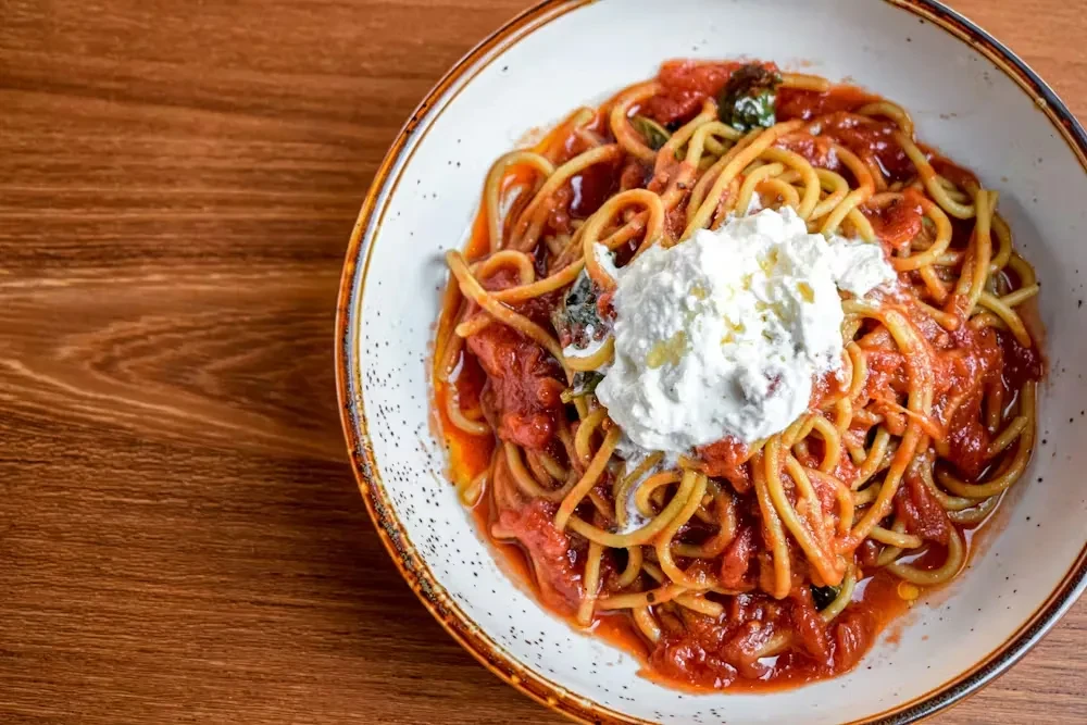 Spaghetti with tomato sauce, creamy cheese, and herbs in a white bowl.