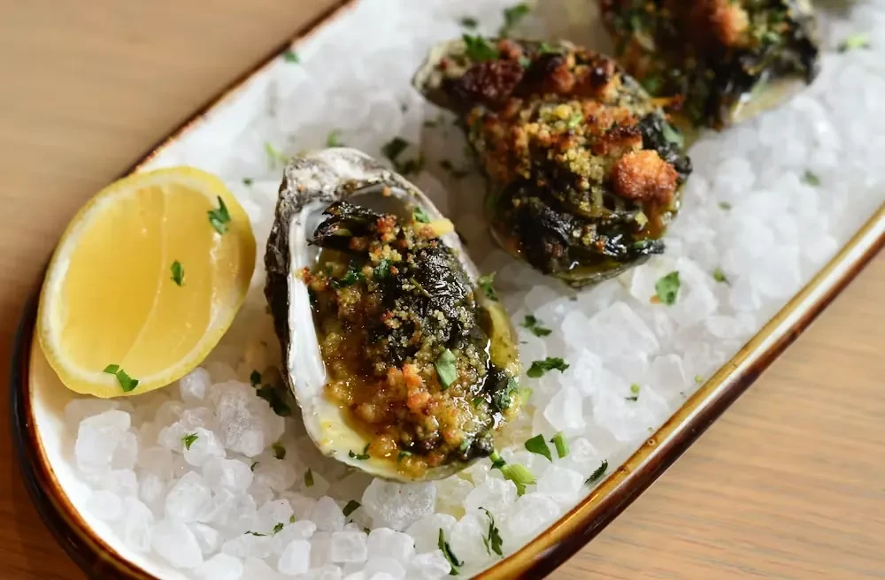Baked oysters on the half shell with lemon wedge and herbs.
