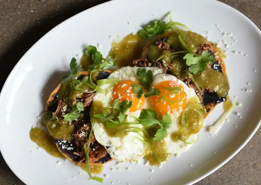 Two fried eggs, tortillas, meat, salsa, and cheese on a plate.