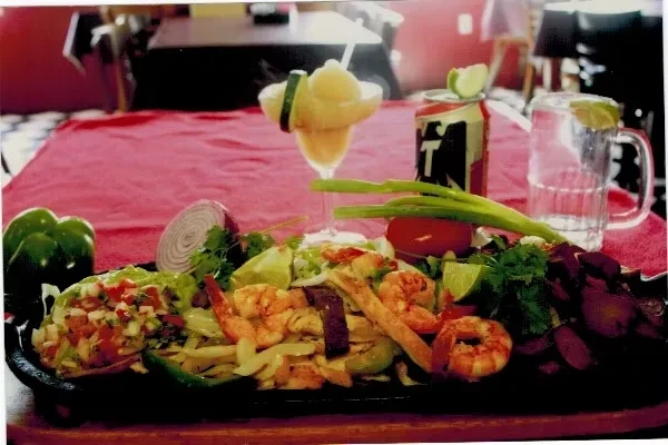 Fajitas with shrimp, chicken, vegetables, and garnishes on a platter.