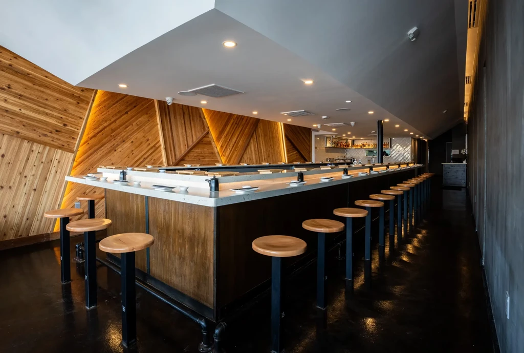 Modern sushi bar with geometric wood paneling and stools.