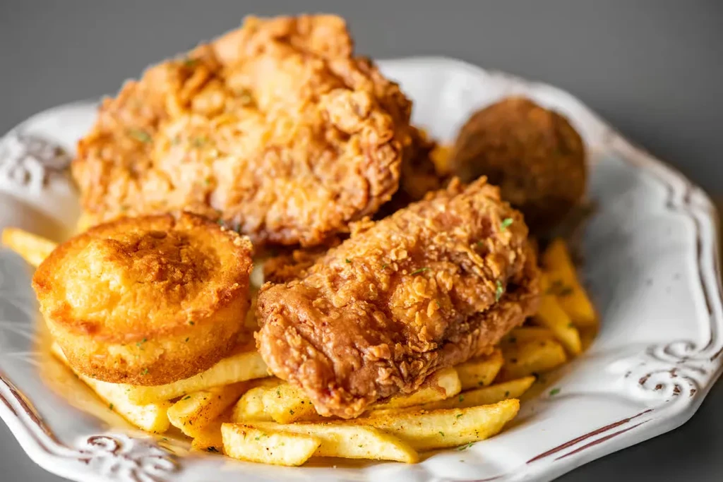 Fried chicken, french fries, corn muffin, and a hushpuppy on a plate.