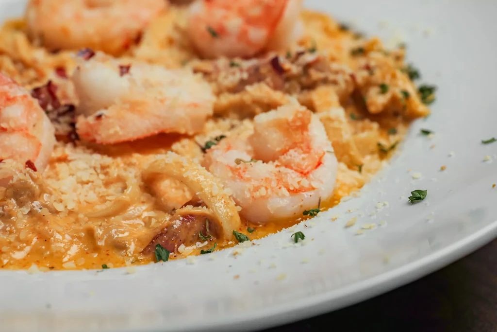 Close-up of a pasta dish with shrimp, creamy sauce, and herbs.