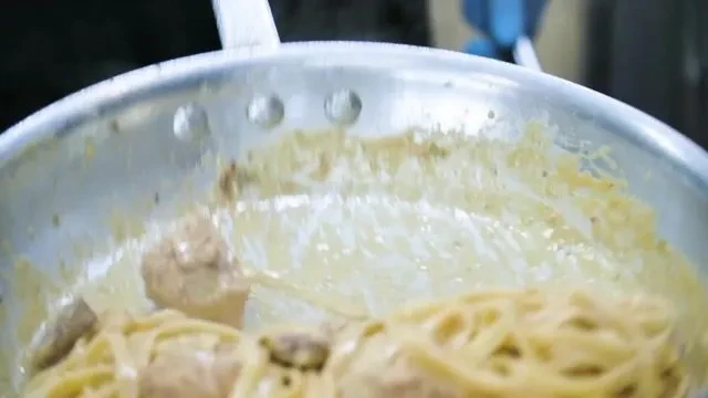 Pasta with creamy sauce and meat cooking in a metal pan.