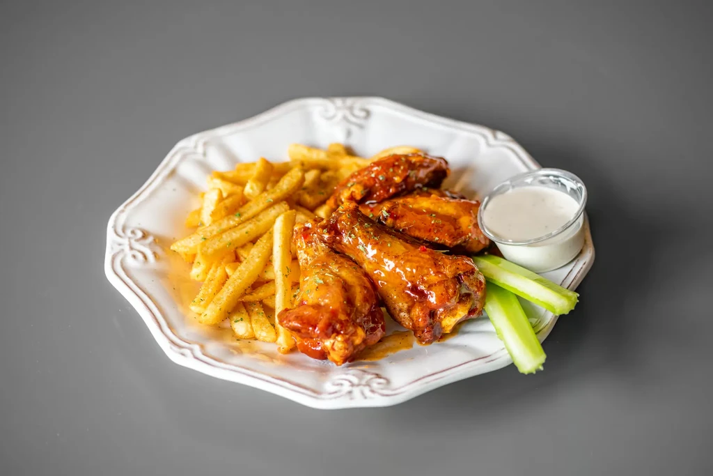 Buffalo wings, French fries, dipping sauce, and celery on a plate.