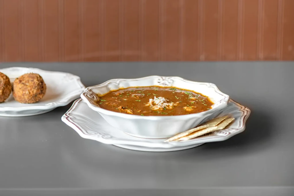 Close-up of a bowl of gumbo with rice, herbs, and crackers.